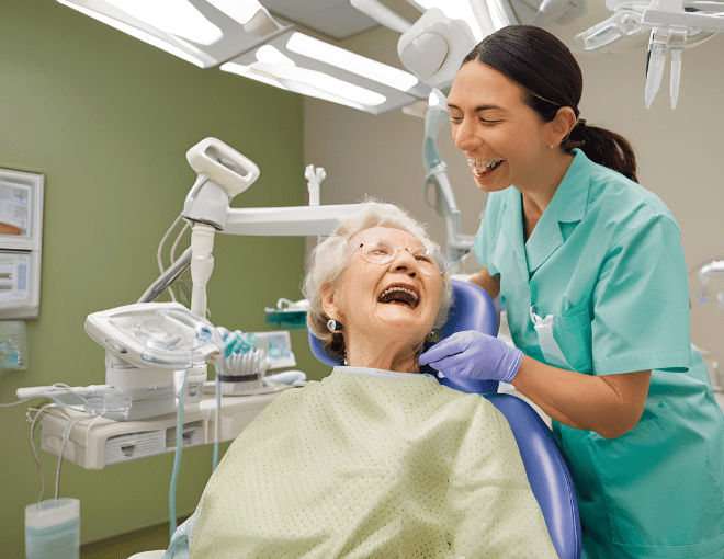 An elderly woman, seated in a dental chair, leans back as a dentist examines her teeth closely, surrounded by bright overhead lights and medical equipment.